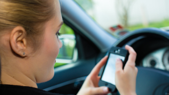 Woman sitting in the driver's seat of her car looking at her mobile phone